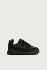 Zapatilla estilo skate color negro, con diseño de volumen, parte superior de piezas combinadas, tira adherente en el empeine y cordones gruesos. Suela con volumen y diseño irregular.