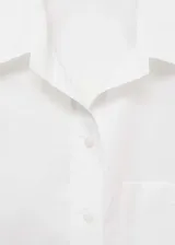 Camisa blanca de popelina de algodón con cuello camisero, cierre de botones, manga larga y detalles fruncidos.
