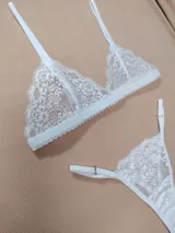 Conjunto de lencería de encaje blanco, compuesto por un soutiene triangular sin relleno con tirantes regulables y una bombacha colaless ajustable con detalles de encaje.