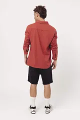 Buzo de algodón tipo polo con cuello camisero, cierre frontal con botones y mangas largas. Presenta un diseño liso en color terracota con logo bordado sutil en el pecho.