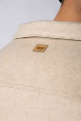 Campera corta tipo sobrecamisa de paño elastizado color beige, con cuello camisero, cierre frontal con botones veteados y dos bolsillos frontales con tapa.
