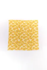 Pañuelo cuadrado de tela ligera con estampado floral en tonos amarillo y blanco con detalles en violeta.