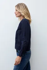 Blusa blanca de manga larga con cuello redondo, confeccionada en tela liviana con detalles de encaje vertical y bordado floral en el pecho.
