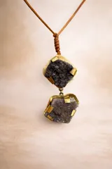 Collar con tiento de cuero marrón ajustable y dos dijes colgantes de druza (geoda) de cristal oscuro, engarzados en metal dorado con detalles de láminas metálicas.