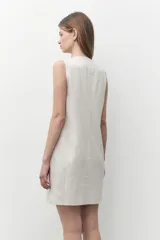 Vestido corto color beige melange, de corte sastrero y confeccionado en lino. Presenta escote en V, cierre frontal con botones y un bolsillo de parche en el pecho.