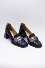 Zapato de cuero negro con aplique plateado y botones forrados en cuero.