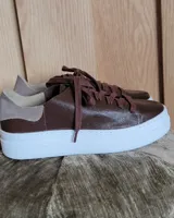 Zapatillas plateadas de cuero con cordones grises y suela blanca.