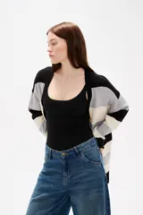 Saco de punto con diseño de rayas horizontales en negro, gris y blanco. Presenta cuello en V, cierre frontal con botones y bolsillos laterales.