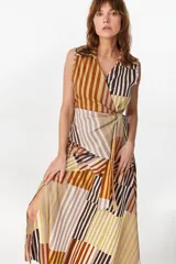 Blusa cruzada sin mangas de algodón, con diseño de rayas verticales y diagonales en tonos tostado, marrón, blanco y ocre. Cuenta con cuello tipo solapa y lazada lateral para anudar a la cintura.