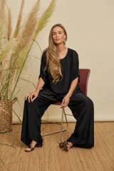 Conjunto de dos piezas compuesto por una blusa de corte holgado con mangas cortas y un pantalón de pierna ancha, ambos en color negro con acabado satinado.