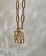 Collar de plata con cadena de eslabones alargados y dije de medalla rectangular con textura rústica, grabado en relieve con forma de estrella y una piedra brillante incrustada en el centro.