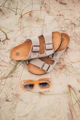 Sandalias de cuero sintético color beige con doble tira y hebillas metálicas ajustables.