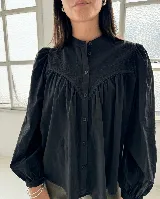 Camisa blanca de algodón con cuello mao, mangas largas con puños elásticos y cierre frontal de botones. Presenta un diseño con pliegues frontales y detalles bordados en la parte superior del pecho.