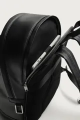 Mochila de diseño minimalista en color negro, confeccionada en material sintético con acabado grabado. Cuenta con un compartimento principal con cierre de cremallera, un bolsillo frontal con cierre y un compartimento posterior acolchado para dispositivos electrónicos. Incluye asa de mano superior y dos correas de hombro ajustables.