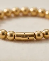 Pulsera esclava de acero con baño de oro, compuesta por pequeñas esferas metálicas unidas en un diseño elástico.