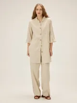 Camisa de lino de silueta relajada y largo irregular, color beige, con cuello mao con volados, botones frontales y mangas tres cuartos con volados en los puños.