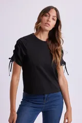 Remera negra de manga corta con cuello redondo y fruncidos ajustables mediante cordones en las mangas.
