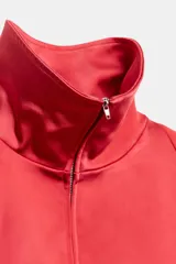 Cazadora roja de satén con cuello subido, manga larga con hombreras, bolsillos delanteros con cierre, bajo ajustable con cordón elástico y cierre frontal de cremallera metálica.