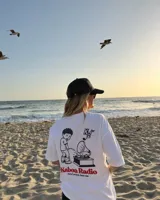Remera blanca de manga corta con estampado gráfico en la espalda que incluye un personaje ilustrado, un gramófono y la inscripción "Kaboa Radio".