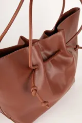 Bolso tipo tote bag negro de cuero sintético, con frunce superior ajustable con cordones y doble asa de hombro.