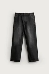 Pantalón de jean estilo carpintero, color negro con efecto lavado, de corte relaxed fit, tiro medio, cierre frontal con botón y cremallera, y bolsillos laterales y traseros.