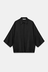 Camisa amplia confeccionada en hilatura con lyocell y ramio, de color negro, con cuello solapa, manga por debajo del codo y cierre frontal con botones ocultos.