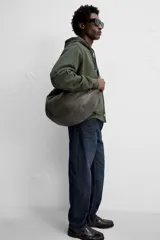 Bolso de hombro tipo media luna, fabricado en piel craquelada color marrón oscuro. Tiene un compartimento principal con cierre de cremallera y un bolsillo interior también con cremallera.