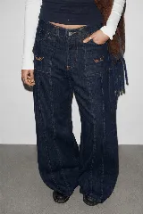 Pantalón de jean azul oscuro de corte baggy, con tiro medio, bolsillos frontales aplicados con detalles bordados y costuras verticales destacadas a lo largo de las piernas.