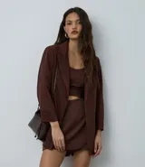 Blazer de sastrería color marrón chocolate, de corte oversized y largo. Presenta solapas clásicas, bolsillos delanteros y detalle de pliegues en los puños. Confeccionado en tejido crepé con forro interior.