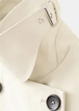 Chaqueta larga de algodón color beige, de diseño recto con cuello en pico y solapas con muesca. Cuenta con cierre delantero de doble botonadura, bolsillos laterales y mangas largas reversibles.