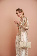 Clutch dorado con forma de moño, cubierto de perlas de diferentes tamaños y cadena dorada.