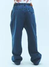 Pantalón de jean azul de corte babucha, tiro medio, con elástico en la cintura, bolsillos delanteros y logo bordado en amarillo en la pierna derecha.