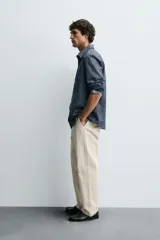 Pantalón chino de algodón color beige claro, corte recto, con cierre frontal de cremallera y botón, bolsillos delanteros y bolsillos traseros de doble vivo con botón.