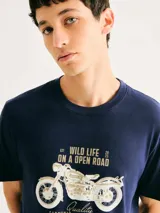 Camiseta blanca de algodón con cuello redondo y mangas cortas. Estampa rectangular con borde negro que contiene la frase "NATURAL ATMOSPHERE" en letras mayúsculas y una imagen de montañas y mar.