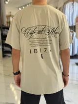 Remera oversize color beige, con mangas corta y gran estampado gráfico en la espalda con texto en negro.