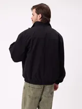 Campera Rusty de corte clásico, color negro, con cierre frontal completo, cuello alto y puños elásticos. Presenta un diseño minimalista con el logo de la marca bordado en el pecho.