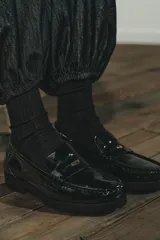 Mocasín de estilo penny en material sintético con acabado acharolado brillante. Presenta un diseño de punta redonda, antifaz clásico en el empeine y una suela dentada robusta.