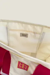 Bolso tote de tela canvas color crudo con asas largas a contratono color fucsia. Presenta un logo estampado al frente en color fucsia.