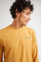 Remera de manga larga color mostaza, con cuello redondo y estampado frontal con las siglas MST en contorno verde.