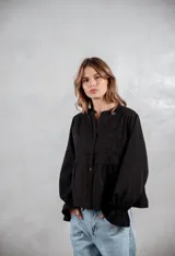 Camisa negra de corte holgado con detalles de bordado tipo broderie en el pecho y mangas largas con puños acampanados.