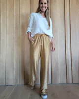 Pantalón de corte holgado y tiro medio, confeccionado en tejido brillante color dorado con acabado metalizado. Presenta cintura elástica con cordón ajustable y bolsillos laterales.
