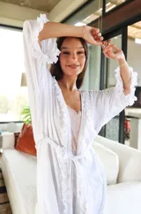 Bata tipo kimono de algodón blanco, con diseño de volados en los bordes frontales y en las mangas. Presenta mangas al codo y un lazo ajustable en la cintura.