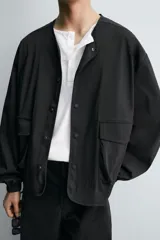 Cazadora de corte boxy fit confeccionada en tejido técnico. Presenta cuello redondo, cierre frontal con botones a presión, mangas largas con puños elásticos y bolsillos tipo plastrón con solapa en la parte frontal.