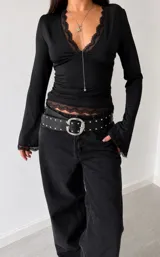 Remera negra de manga larga con escote en V profundo y detalles de encaje en el borde del escote, puños y ruedo. Presenta un diseño entallado y femenino.