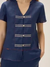 Camisa azul marino de lino, de corte holgado y manga corta, con cuello en V y detalles de galones decorativos con botones frontales.