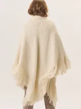 Triángulo de lana color beige con maxi flecos, diseñado por Margara Shaw en colaboración con Manos del Uruguay. Confeccionado con una mezcla de lana merino, mohair, viscosa, algodón y otras fibras, incluyendo lurex y un hilado teñido a mano con lentejuelas.