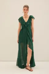 Vestido largo cruzado color verde esmeralda con pequeños puntos dorados metalizados. Presenta escote en V con volados en el borde y mangas cortas con volados. La falda tiene un corte asimétrico con abertura frontal.