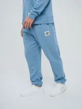 Pantalón jogger celeste de felpa, con cintura elástica ajustable con cordón, puños elastizados en los tobillos y un parche con el logo de la marca en la pierna izquierda.