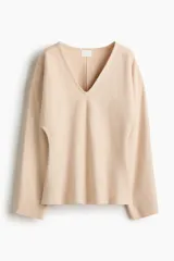 Remera de punto fino suave color beige con escote en V, modelo de cintura entallada con mangas dolman largas.