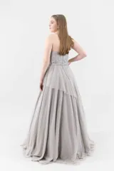 Vestido largo de fiesta color visón, con escote palabra de honor, corsé armado de encaje bordado con apliques florales y falda amplia de tul con volados irregulares.